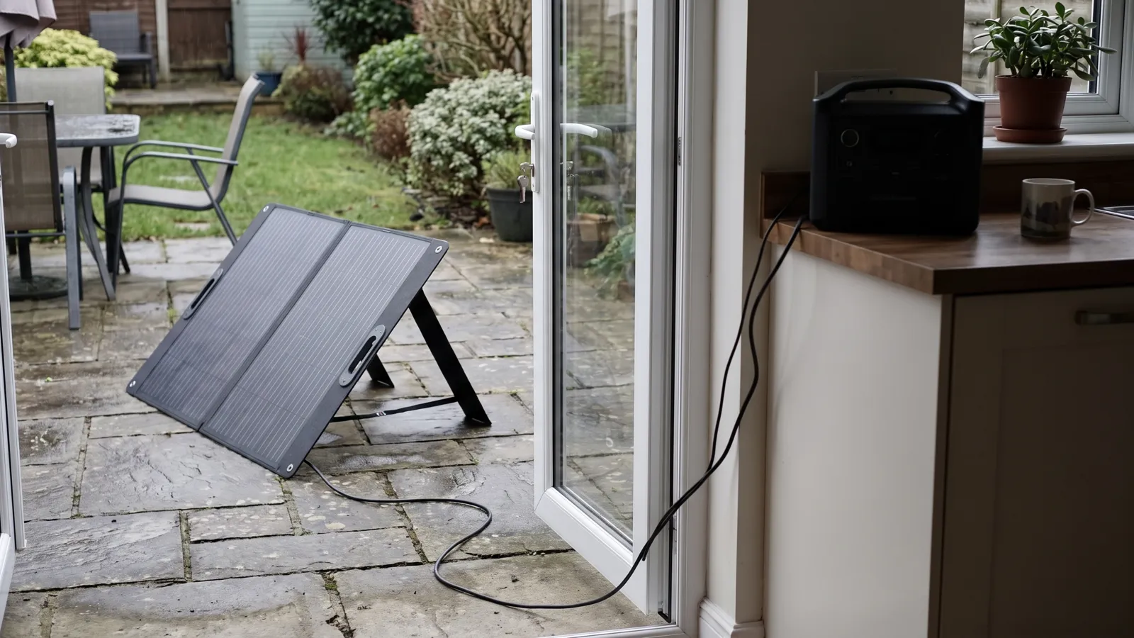 A folding solar panel on a garden patio with its cable running indoors to a power station