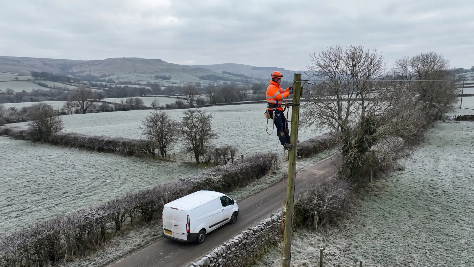 An electricity network engineer working on an overhead line pole in a frosty rural field