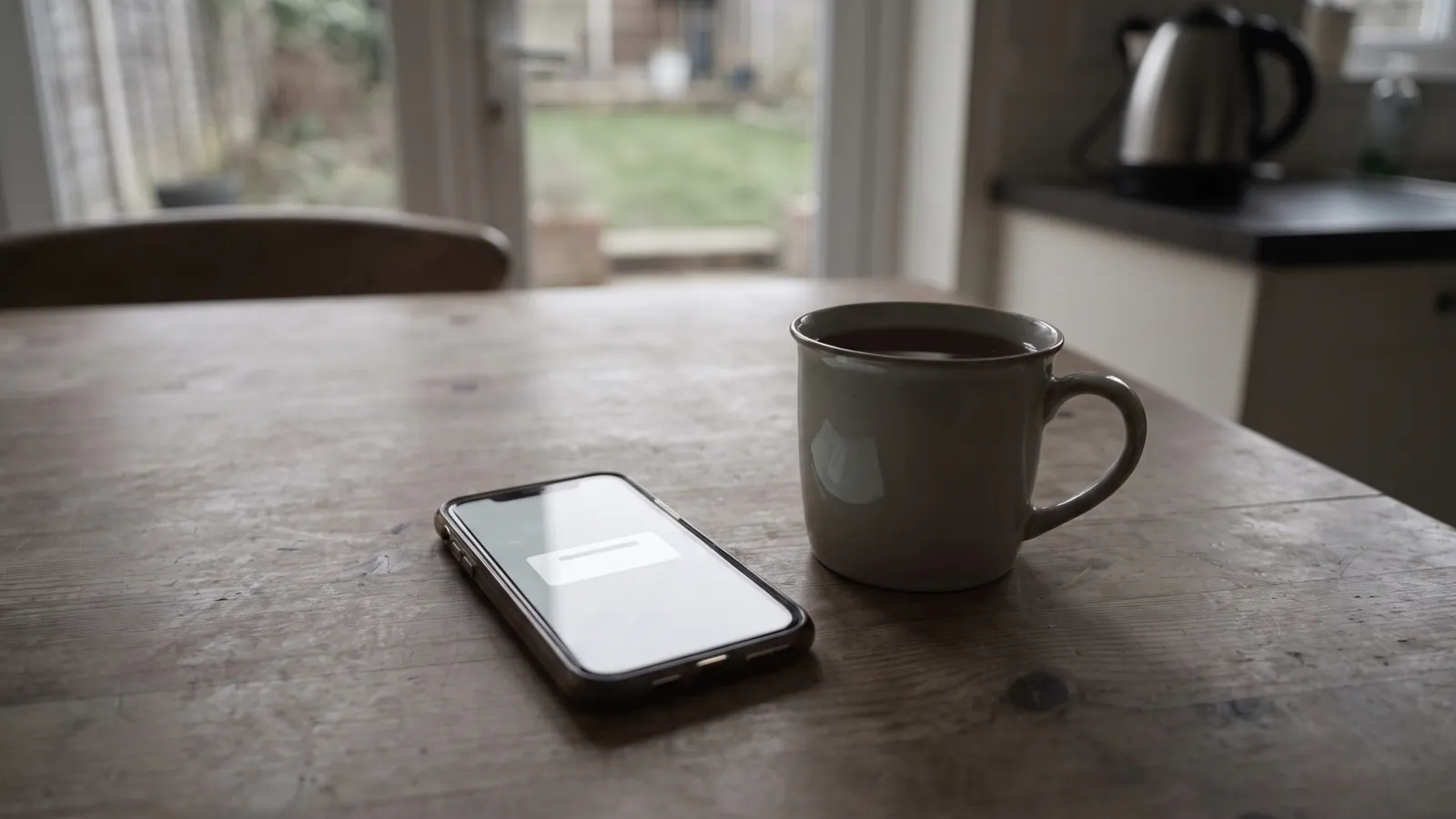 A mobile phone on a kitchen table showing an emergency alert notification beside a mug of tea