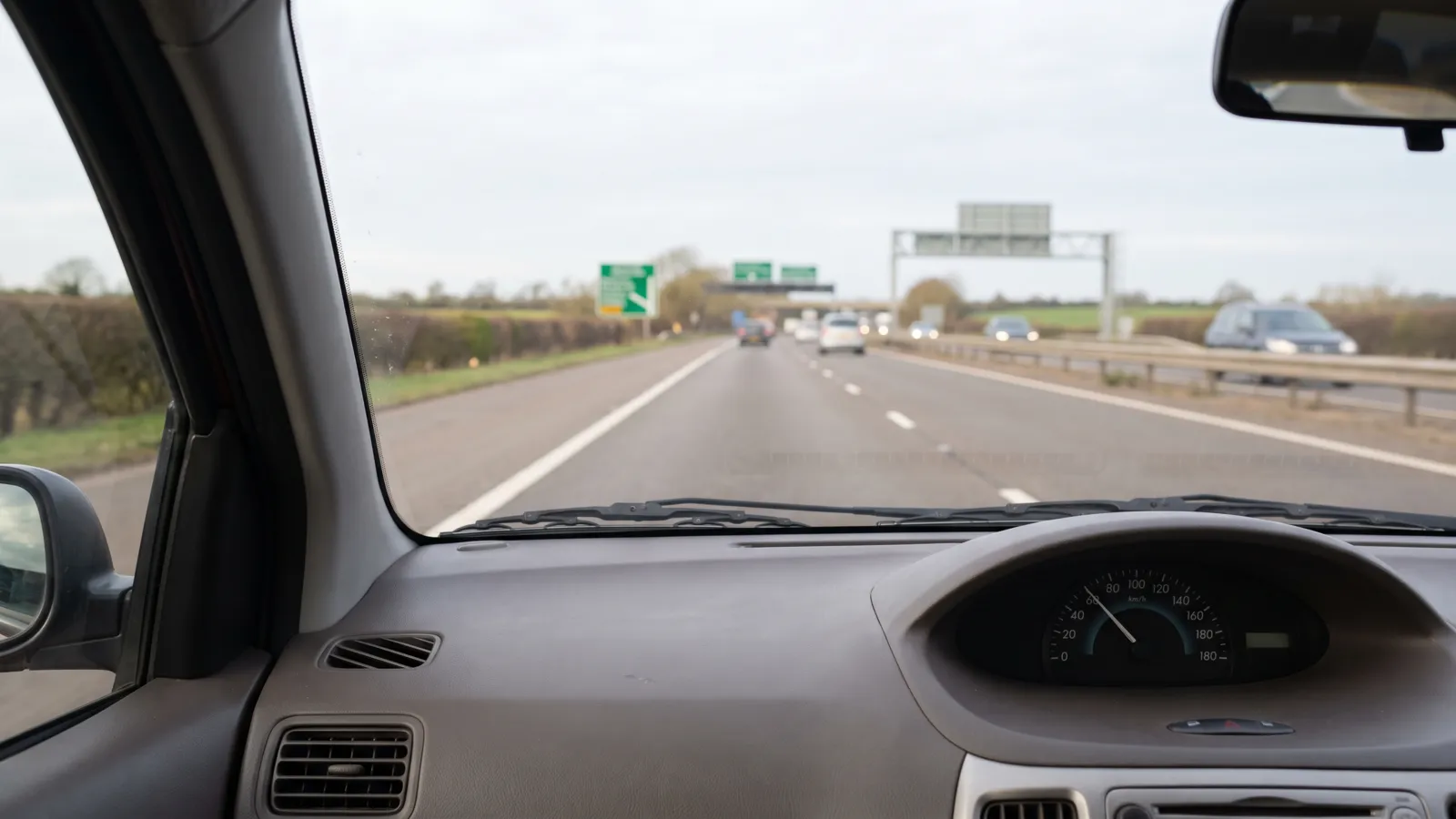A car dashboard showing a steady speed on a clear British motorway in daylight